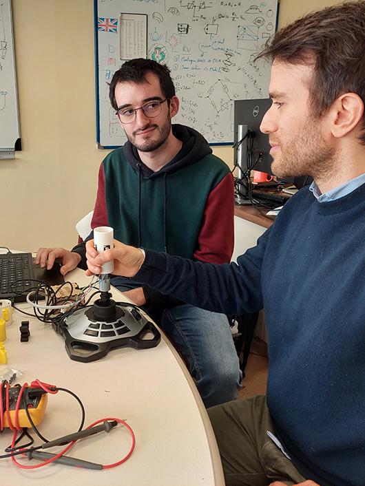 À l’aide de quatre moteurs vibreurs sur un joystick, Pierre-Antoine Cabaret (à gauche) conçoit un système de déplacement dans un dédale. Ici, la vibration indique la direction à prendre. Le joystick servira au pilotage d’un fauteuil électrique. À droite : le chercheur Claudio Pacchierotti.